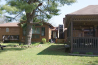 view across yard toward wooden buildings with wooden decks with metal tables, picnic table on lawn