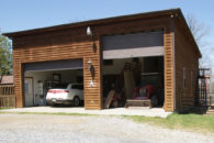 multi vehicle brown wooden garage with brown doors with one sie taller for equipment, gravel driveway