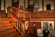 view from great room with pictures on wall and queen anne chair at foot of wide wooden staircase to 2nd level