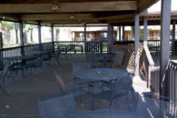 black metal patio tables under covered wooden deck with single level wooden building behind