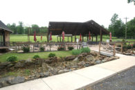 L shaped sidewalk leading to short bridge over creek heading toward patio with tables and red umbrellas