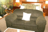 Fron view of oak sleigh bed, olive love seat at foot and coffee table, nightstands with lamps, tan carpet