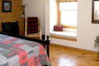 Full bed bed with black footboard with oak rocker in corner, wooden floors, window with white cushioned seat.