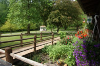 View toward white gazebo under trees from front entrance across ramp with colorful flowering plants on right